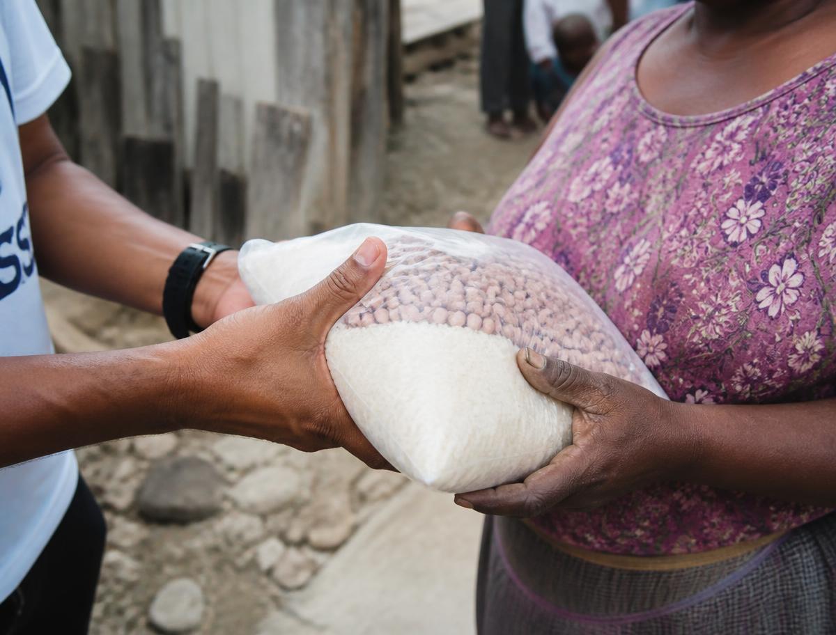 Mãos entregando um pacote de arroz e feijão